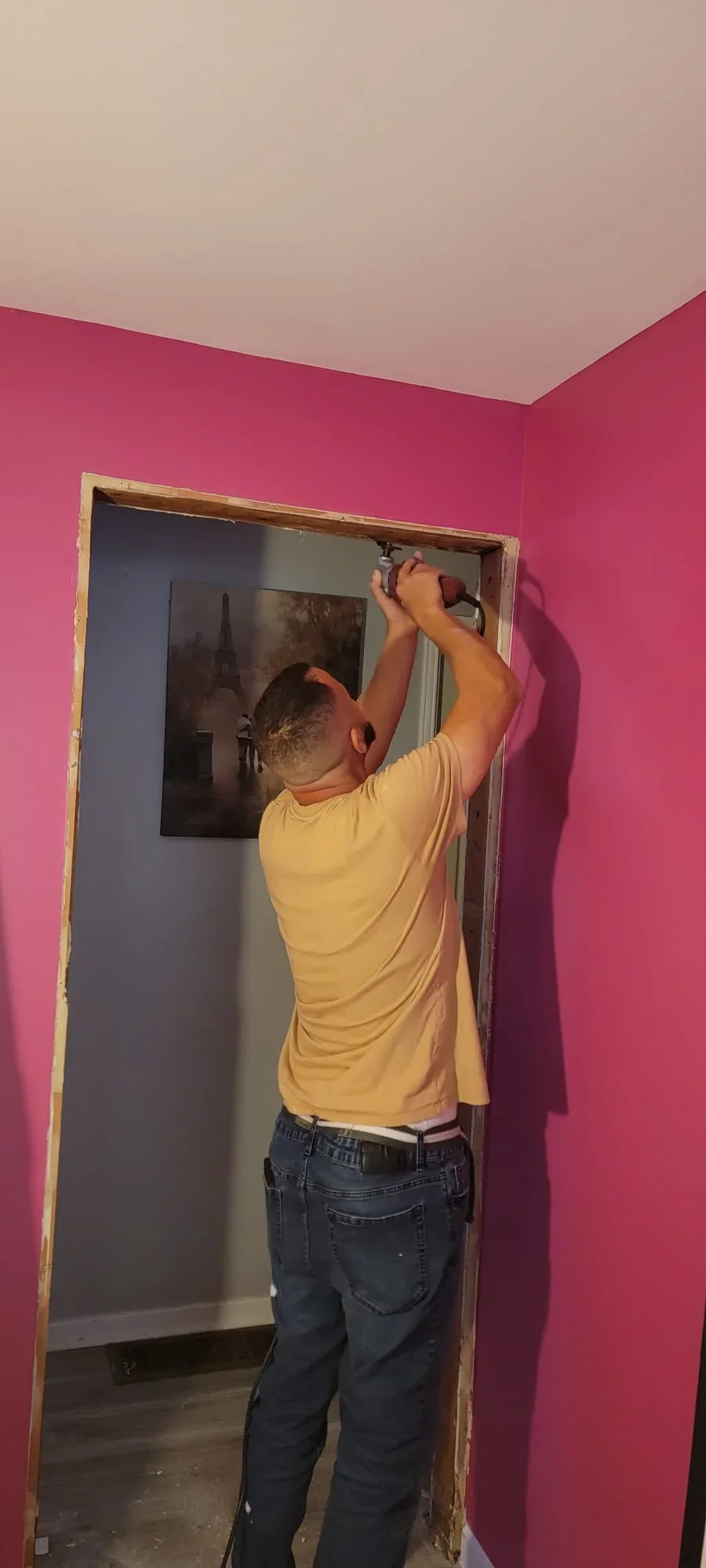 Worker installing wooden door frame in magenta-painted interior room with white ceiling