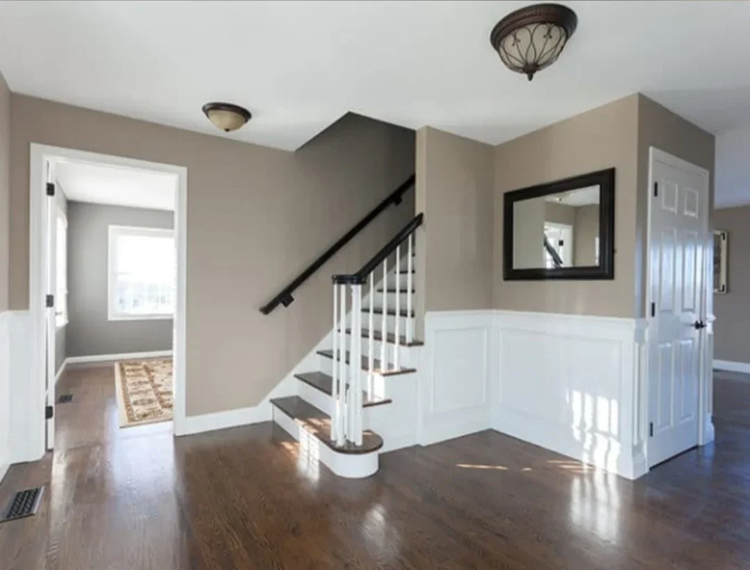 Two-story foyer with taupe walls, white wainscoting, dark hardwood floors, and white staircase with dark handrail