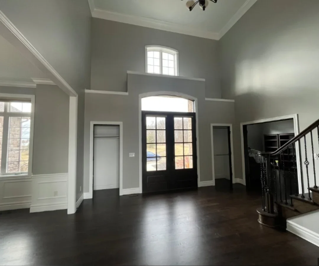 Two-story foyer with gray walls, white trim, dark hardwood floors, and black entry doors