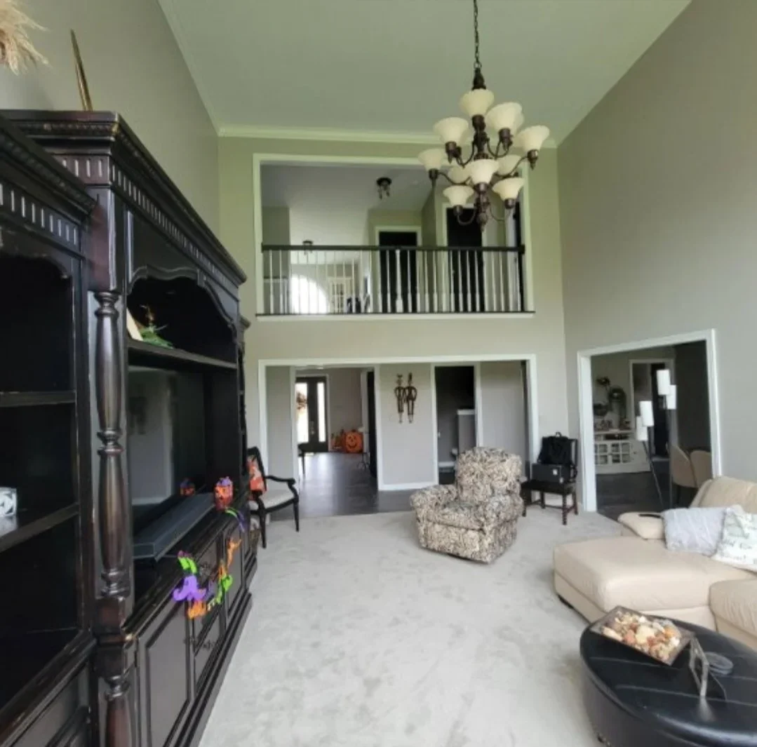 Two-story interior with sage walls, white trim, gray flooring, black fireplace, and upper mezzanine railing